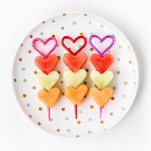 Three Valentine's fruit kabobs on a polka dot plate.
