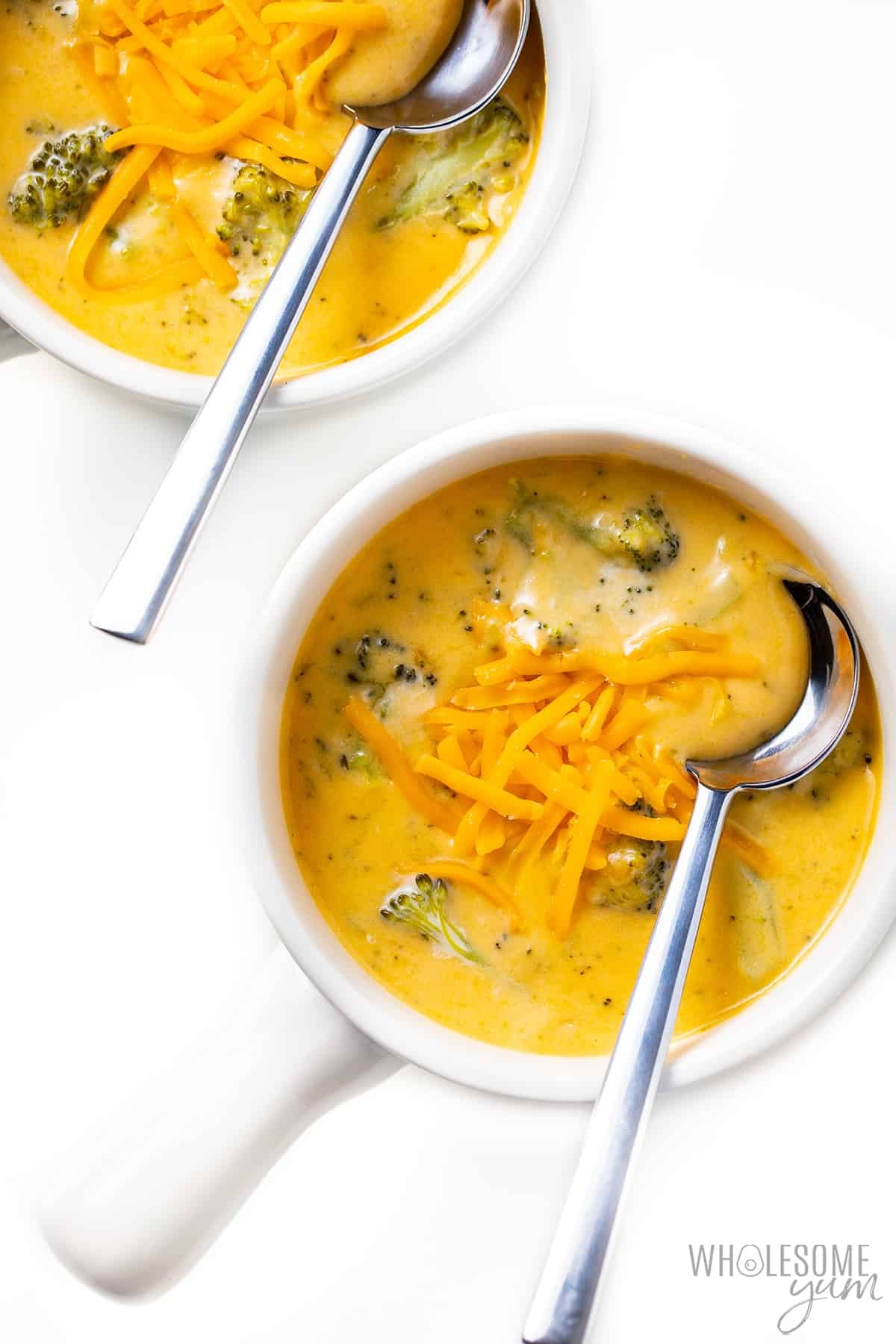 Two bowls of broccoli cheese soup with spoons in them.