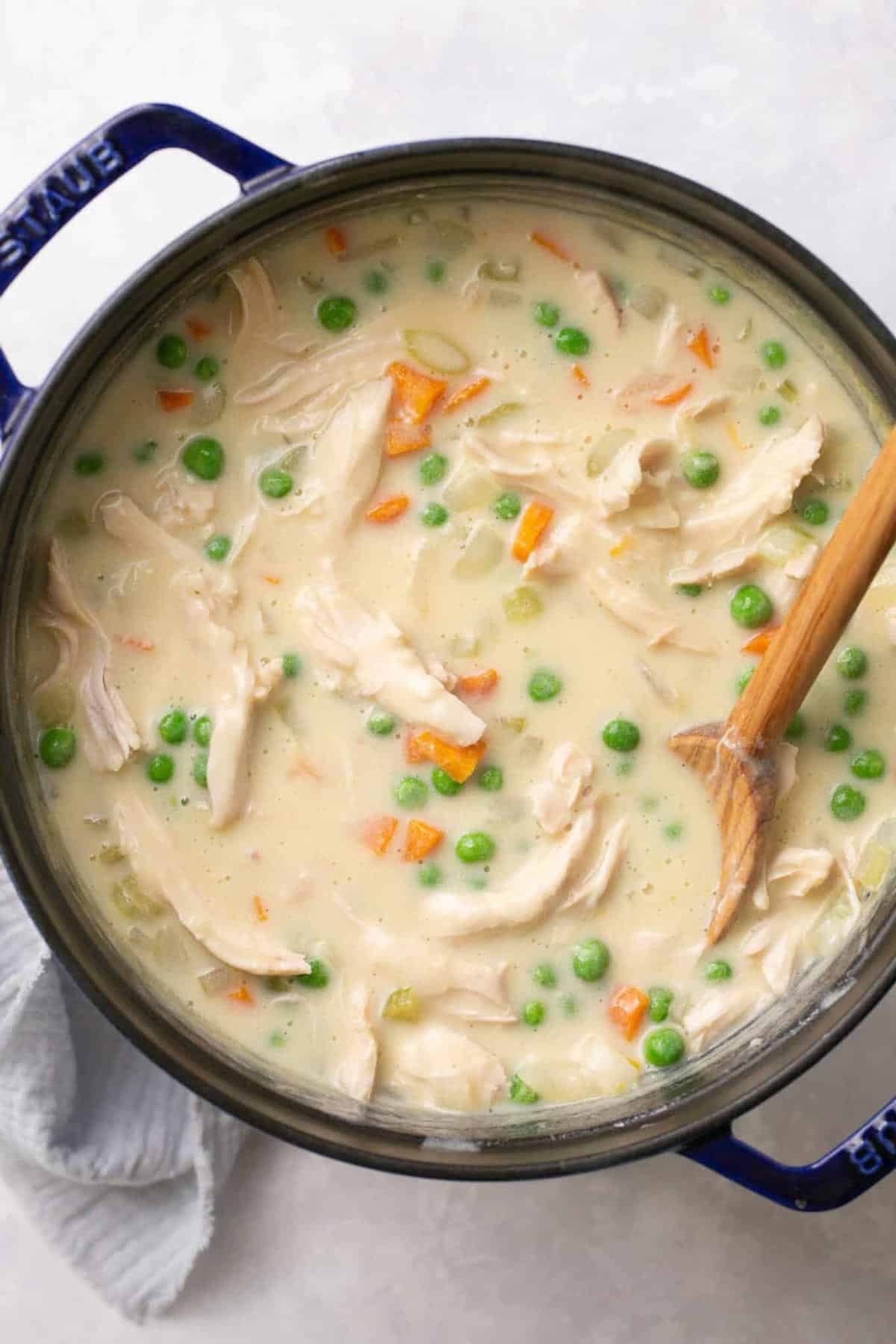 A large pot of healthy chicken pot pie soup with a wooden spoon in it.