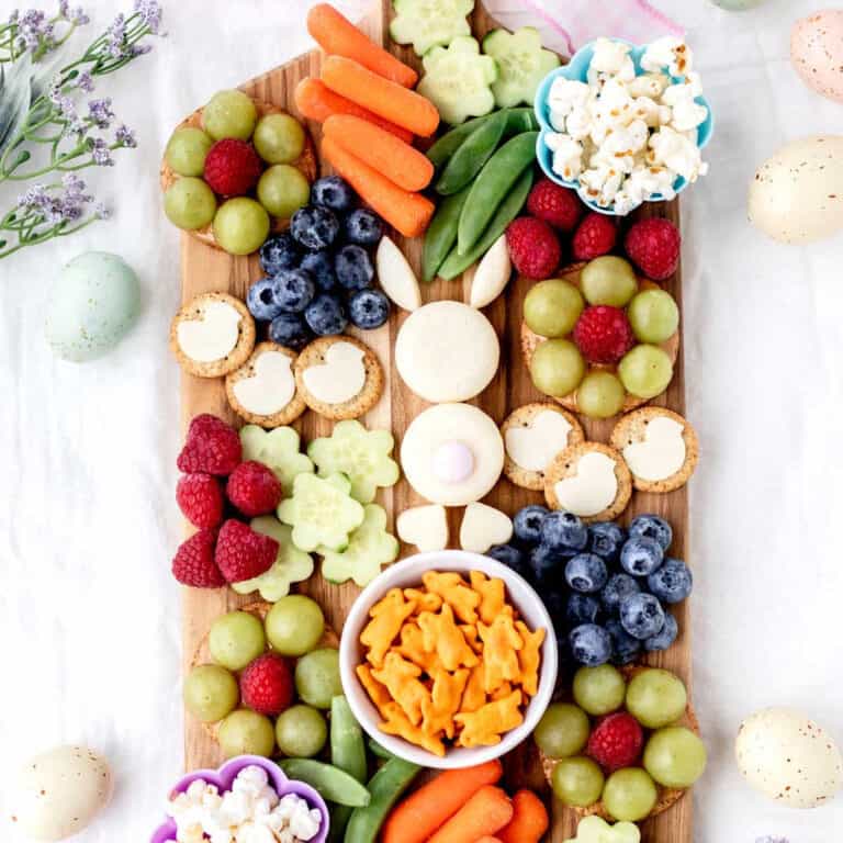 Easter bunny snack board surrounded by flowers and Easter eggs.