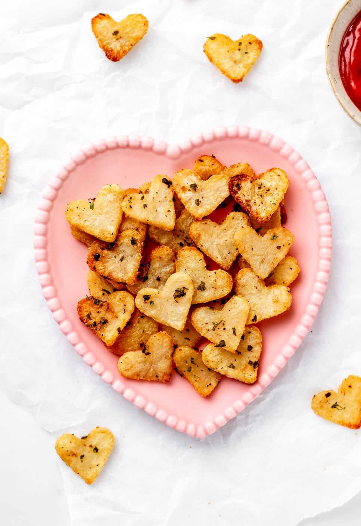 Roasted heart potatoes on a pink heart-shaped plate with ketchup.