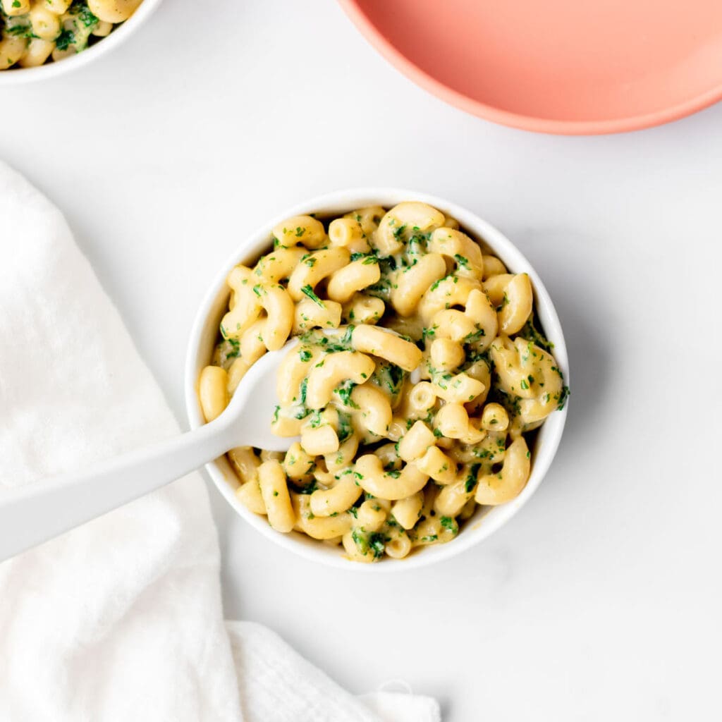 A spoon digging into a small bowl of mac and cheese with kale.