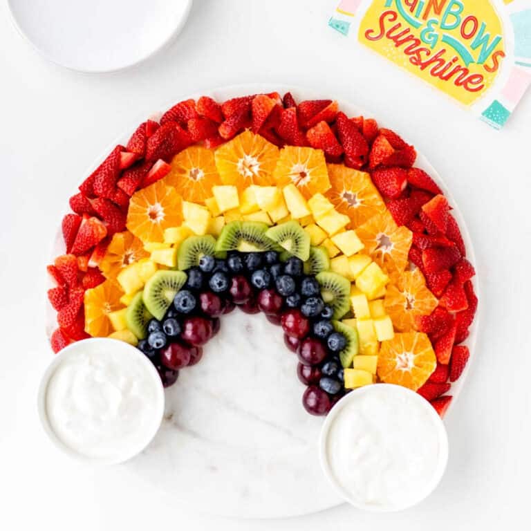 Rainbow fruit board with two bowls of yogurt fruit dip.